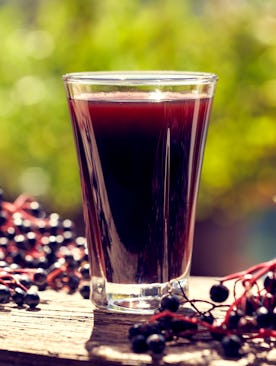 A shot of elderberry syrup with elderberries surrounding it.