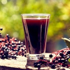 A shot of elderberry syrup with elderberries surrounding it.