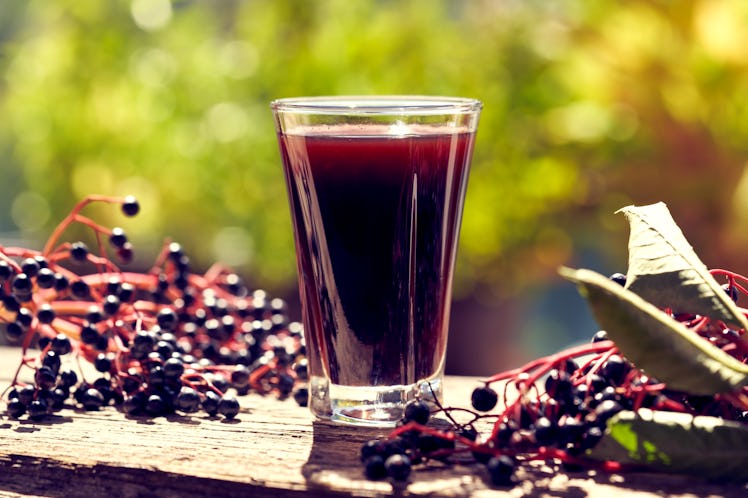 A shot of elderberry syrup with elderberries surrounding it.