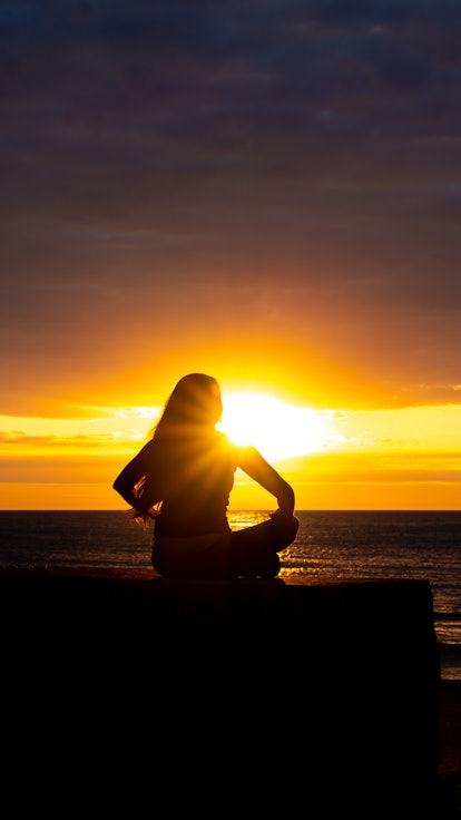 A woman in silhouette doing yoga with the sunrise.