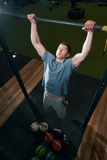 A man doing a dead hang on a pullup bar at a gym.