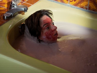 Young woman lying in a full bathtub with blood on her face