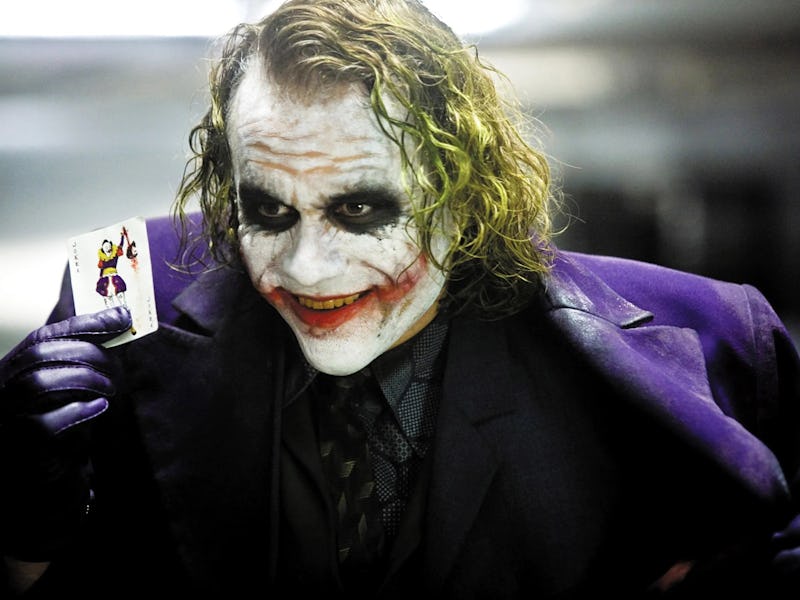 Heath Ledger as Joker, holding a card while smiling in The Dark Knight movie