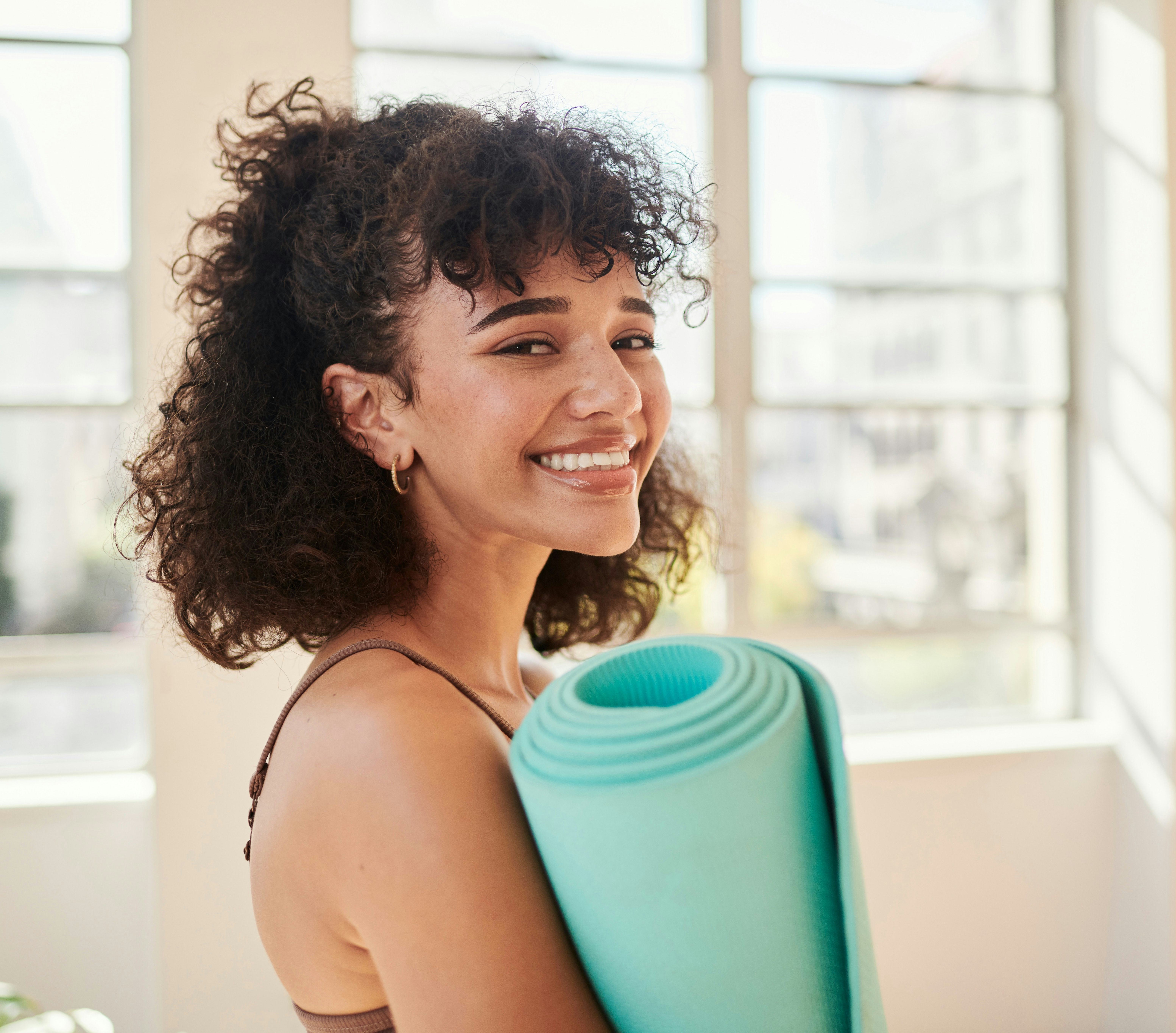 A woman gets ready to follow a guide to Sun Salutations in yoga with her yoga mat at home. 