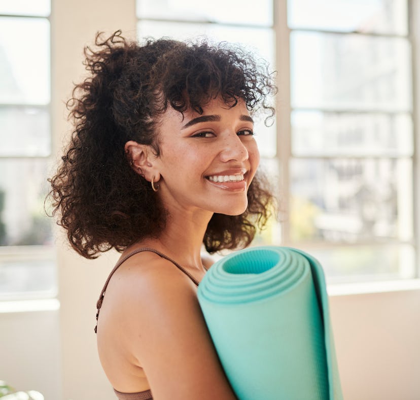 A woman gets ready to follow a guide to Sun Salutations in yoga with her yoga mat at home.