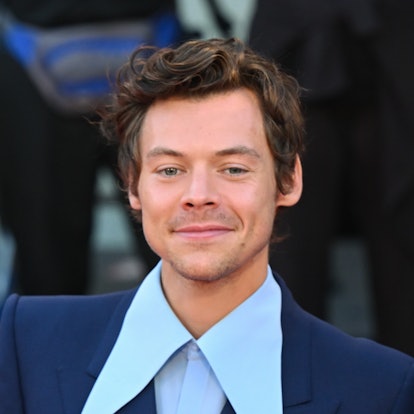 Harry Styles posing with a big smile wearing a blue suit.