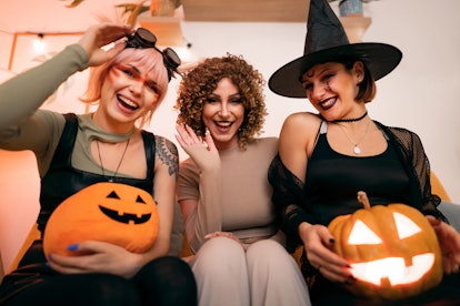 Group of friends holding pumpkins and smiling after hearing their Halloween 2022 horoscope.