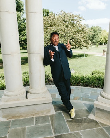 Sammy Stephens leaning against a white pillar while wearing a black suit