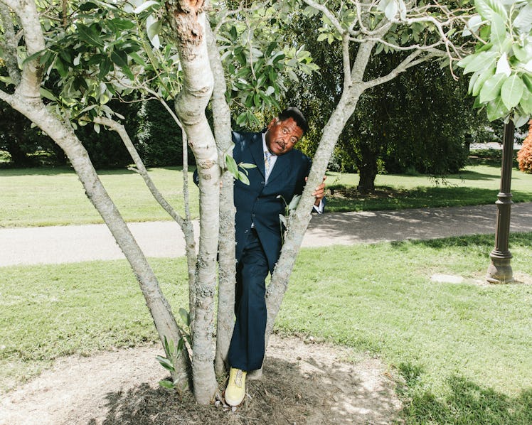 Sammy Stephens standing between tree branches while wearing a black suit