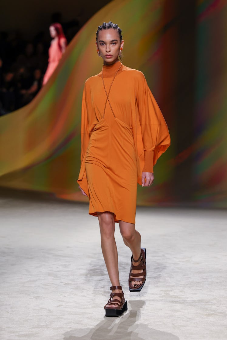 A model wearing Hermès signature orange knee-high puffy long sleeved dress and sandals at Paris Fash...