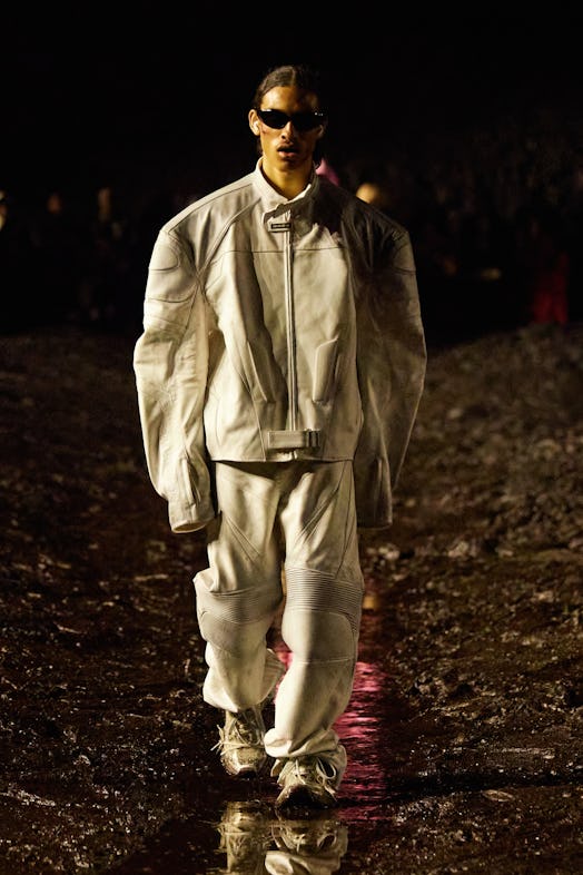 A male model walking the mud Balenciaga show in a white combination of pants and jacket