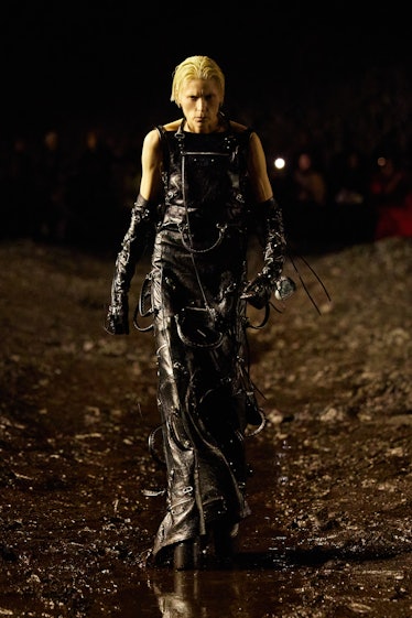 A female model walking the mud Balenciaga show in a black dress with black gloves 