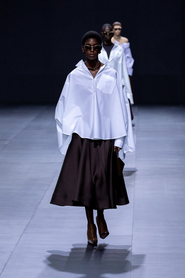 A model walking in Valentino oversized asymmetrical white shirt and black knee-high skirt at Paris F...