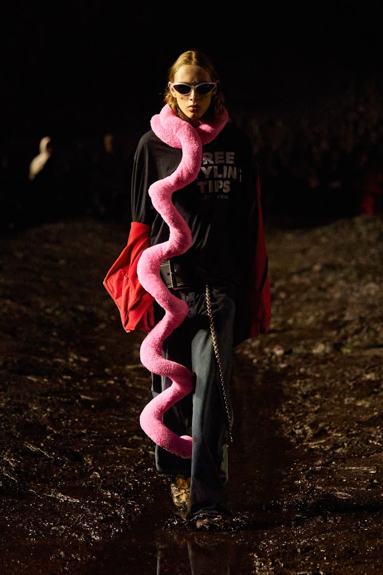 A model in Balenciaga sunglasses, black t-shirt with print, dark loose and pink long scarf at Paris ...