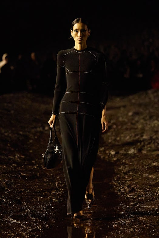 A female model walking the mud Balenciaga show in a black overall dress