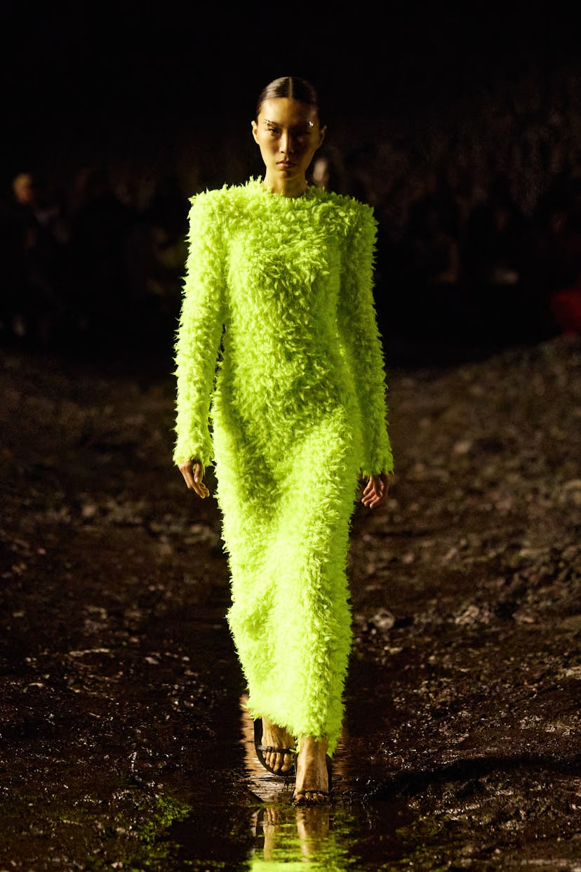 A model walking the muddy runway at Balenciaga in Paris while wearing a bright highlighter yellow lo...