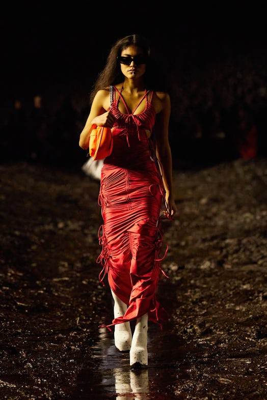 A female model walking the mud Balenciaga show in a red dress and white heel boots