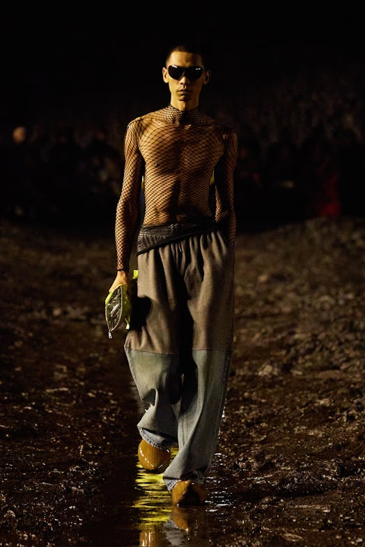 A male model walking the mud Balenciaga show in a see-through black net shirt