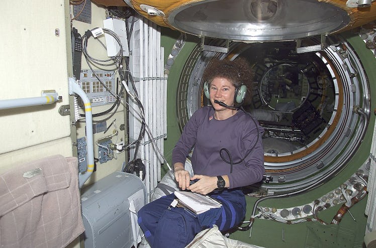 color photo of a woman in a flight suit sitting in front of a large pressurized hatch