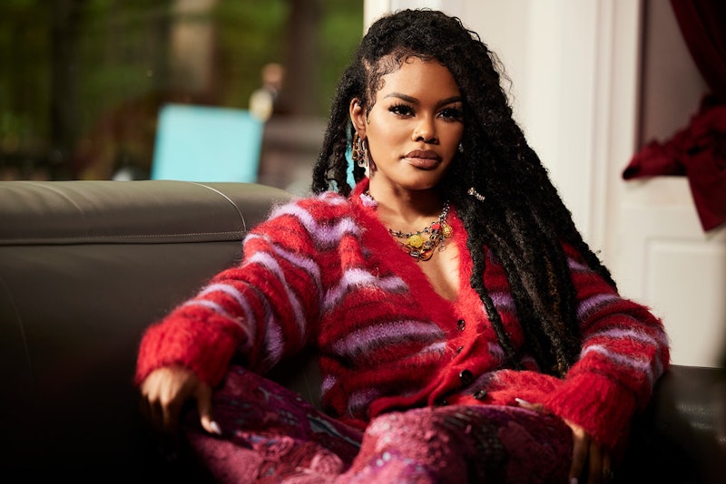 Teyana Taylor in a red and purple striped cardigan and chunky jewelry sitting down for an interview