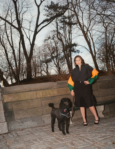 Catherine Cohen standing in front of Central Park in the fall with a black dog