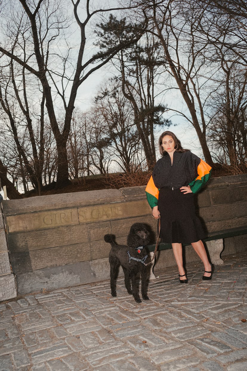 Catherine Cohen standing in front of Central Park in the fall with a black dog