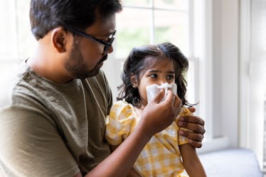 A dad blowing his sick daughter's nose with a tissue.