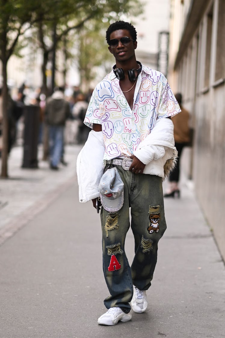 A model is seen wearing a white smiley face print shirt, white jacket, patched jeans and white sneak...