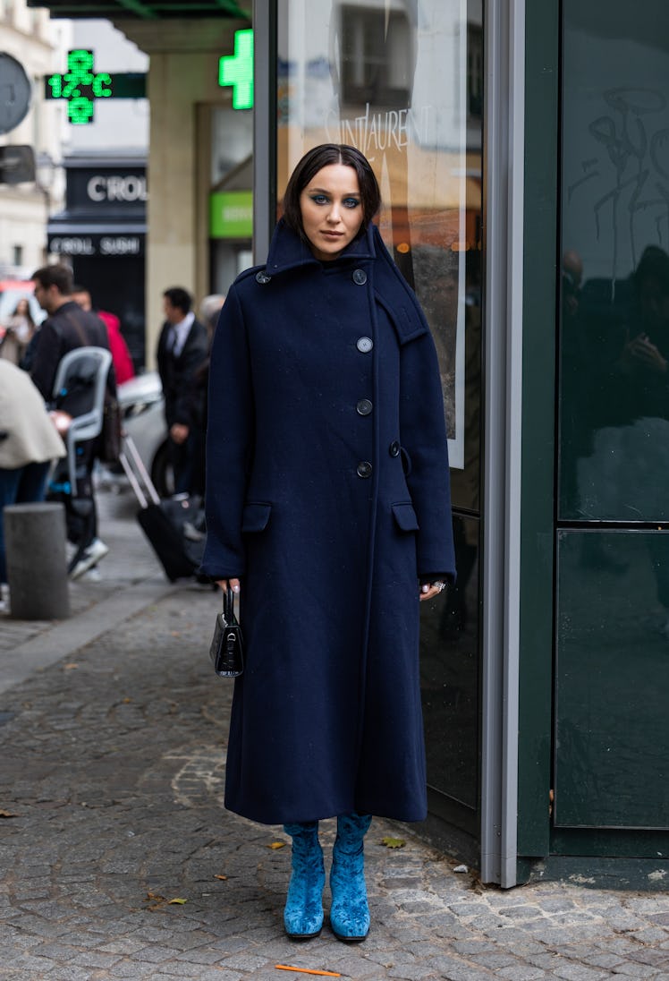 A guest wears button up navy wool coat, blue boots, bag outside Stella McCartney during Paris Fashio...