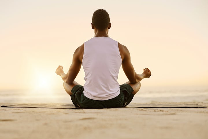 Fit and active man doing yoga, meditating and relaxation exercise on the beach. Calm, peaceful and r...