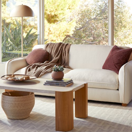 A living room with Parachute furniture, a beige couch with brown pillows, a beige-brown coffee table...