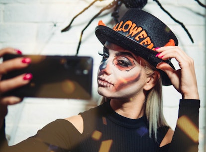Young woman fixing her hat and taking a selfie before posting it on Instagram with a Halloween pun.