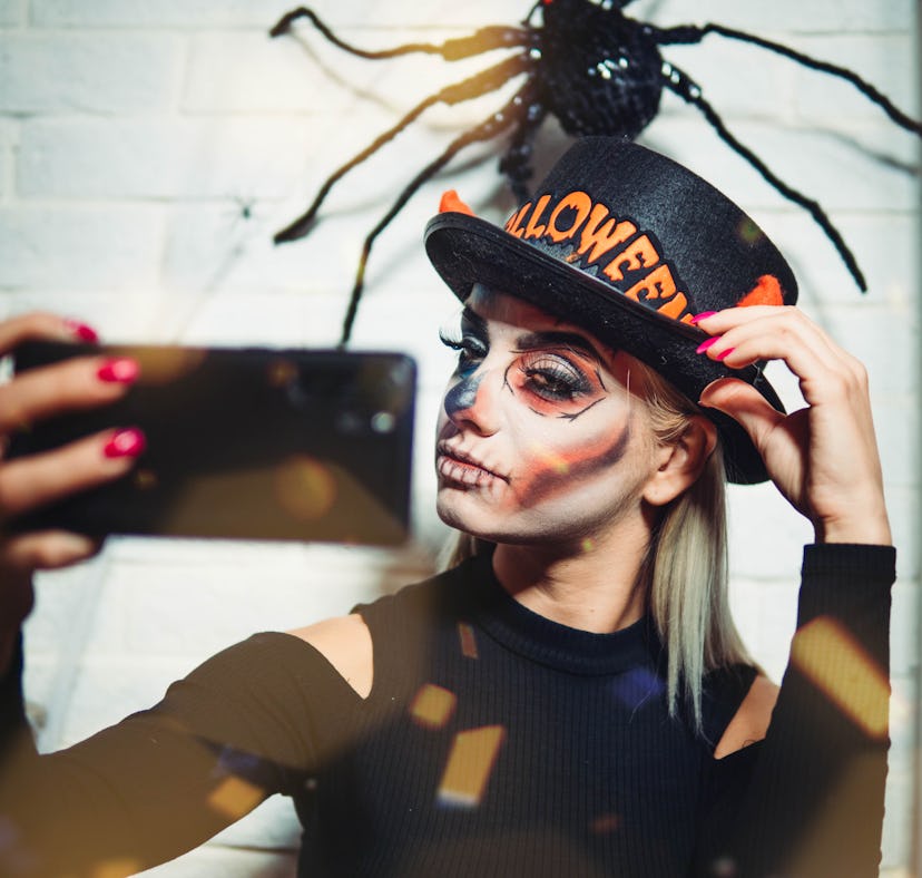Young woman fixing her hat and taking a selfie before posting it on Instagram with a Halloween pun.