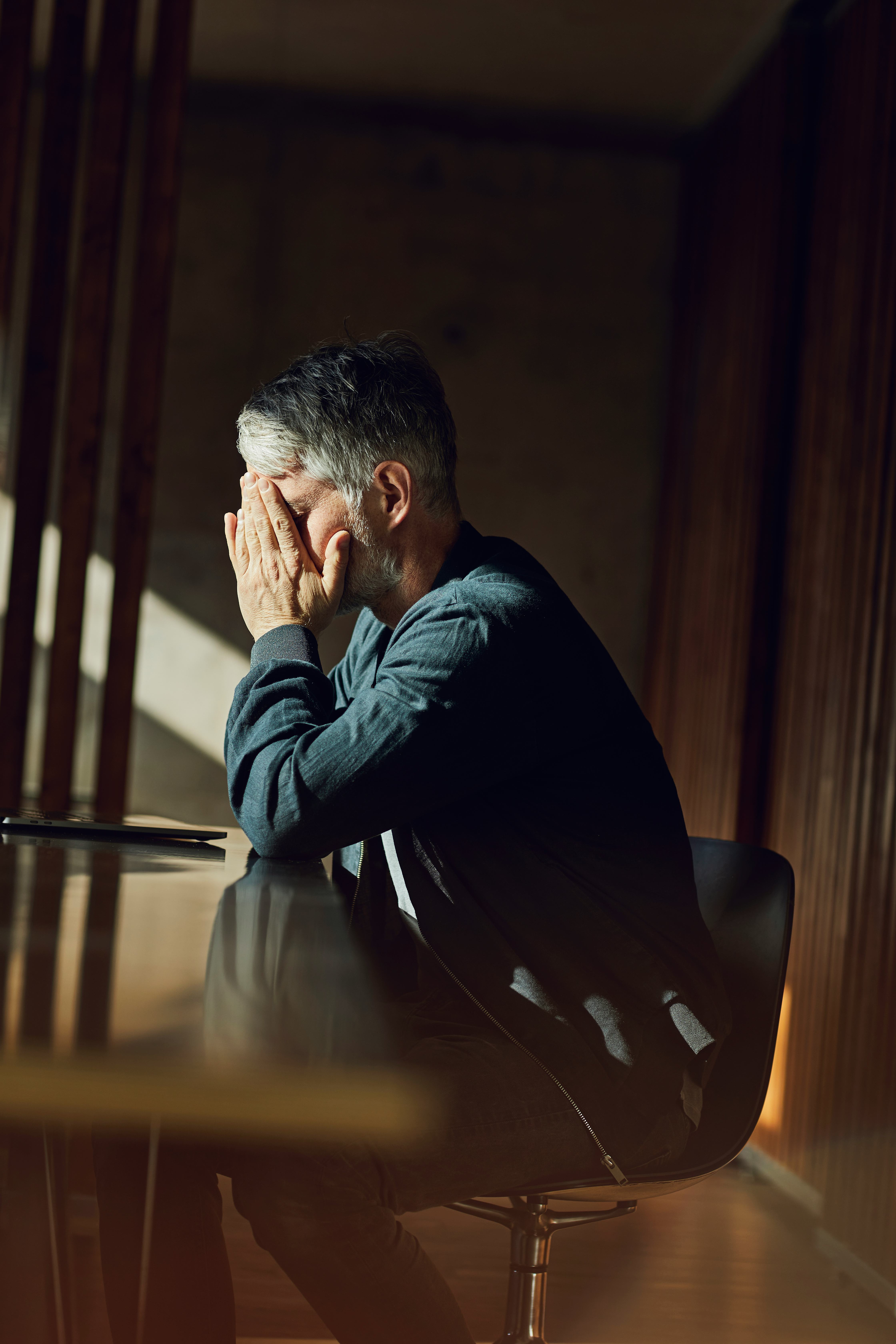 一个男人坐在办公桌前，双手捂着脸。