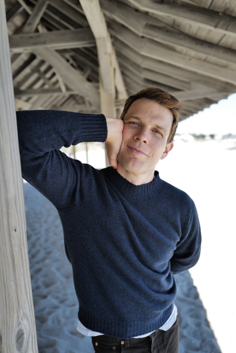 Jake Lacy smiling with his arm resting on a pagoda