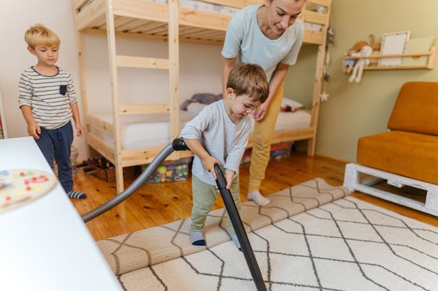 A mom vacuums a rug with her kids.