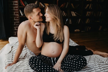 A man and pregnant woman sitting in bed, about to kiss.
