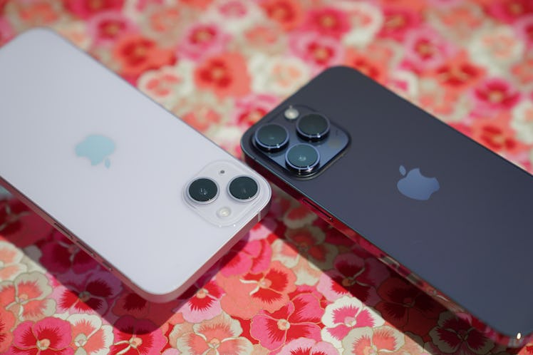 Two iPhone 14 Plus models in black and in white on a table with a floral table cloth 