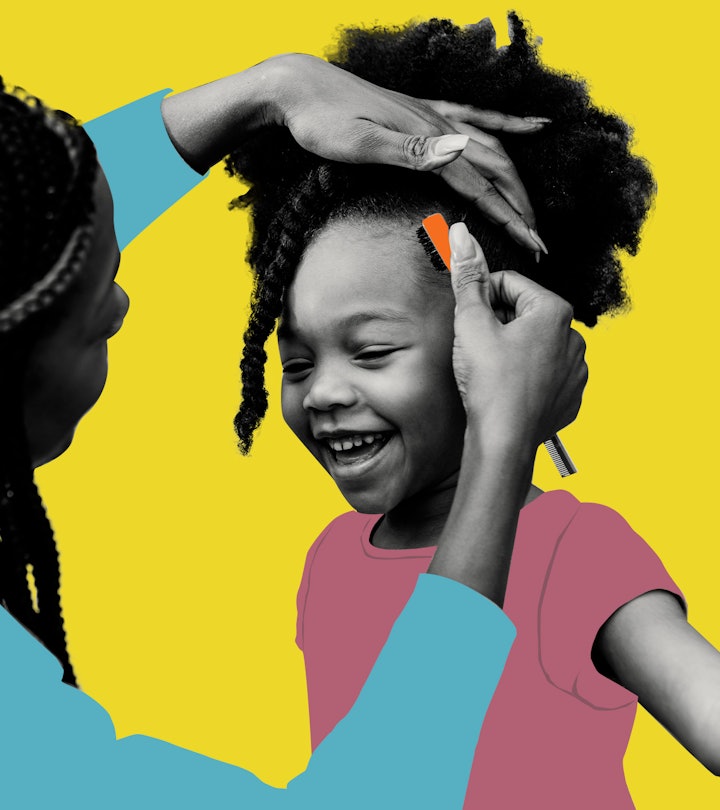A black mother styling her daughter's hair while she is smiling