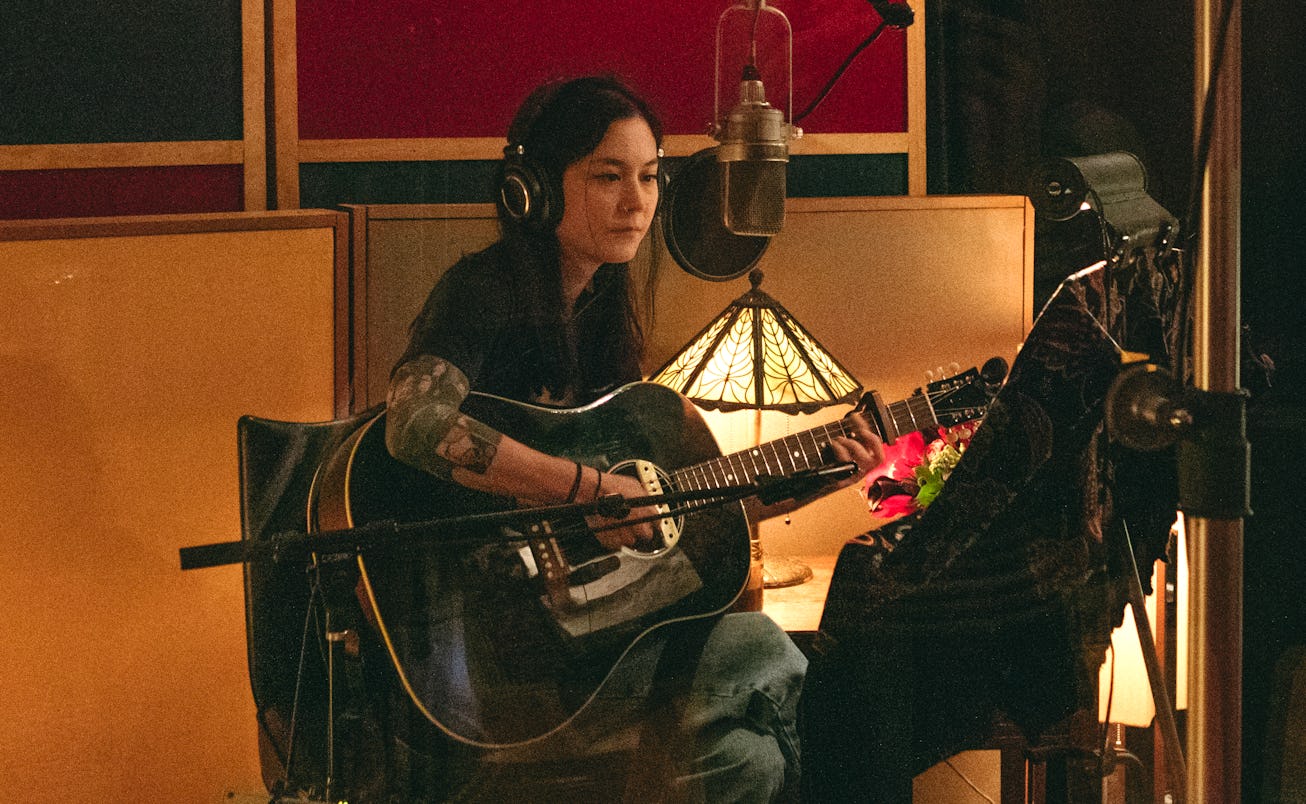 Michelle Zauner playing an acoustic guitar in a studio