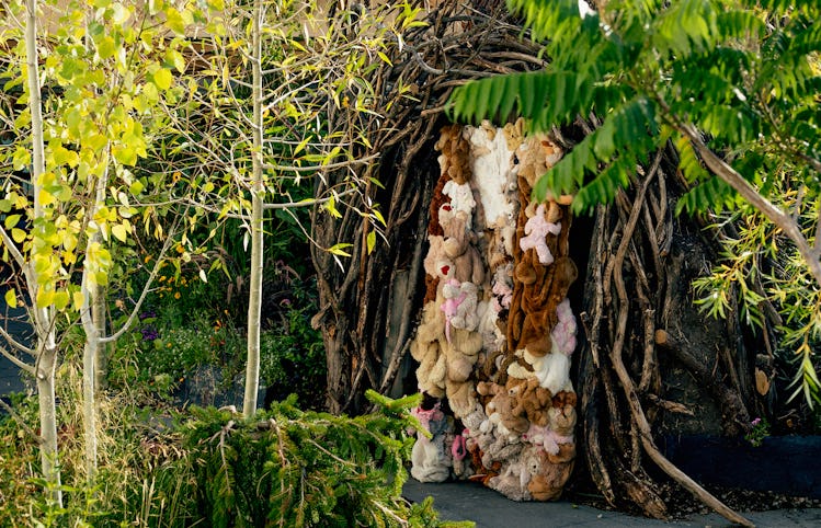 a door covered in stuffed animals adorns a structure made of tree trunks