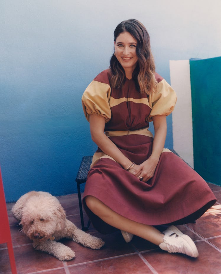 Yam Karkai wearing a Colville maroon and beige dress, her own jewelry, and sneakers, with her dog ne...