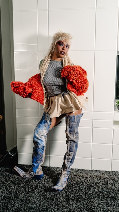 Sudan Archives wearing a red furry knit bolero, a shiny mini skirt, and thigh high boots