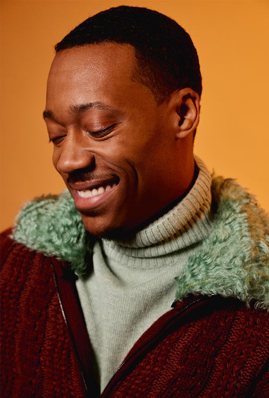 Tyler James Williams smiling in a red jacket and white sweater