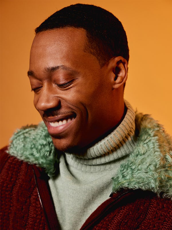 Tyler James Williams smiling in a red jacket and white sweater