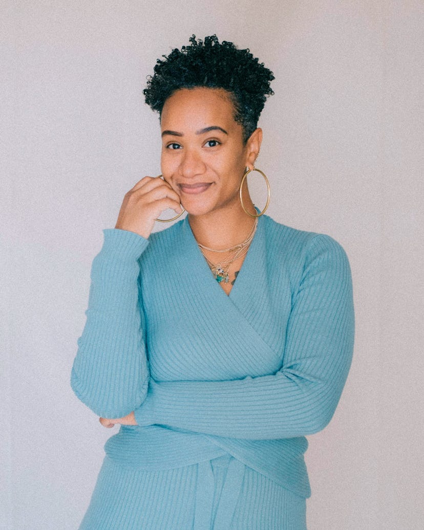 A portrait of Alex Elle wearing a blue wrap sweater, and smiling at the camera