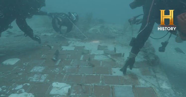photo of two divers examining a piece of wreckage underwater, assisted by a small flock of fish