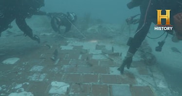 photo of two divers examining a piece of wreckage underwater, assisted by a small flock of fish