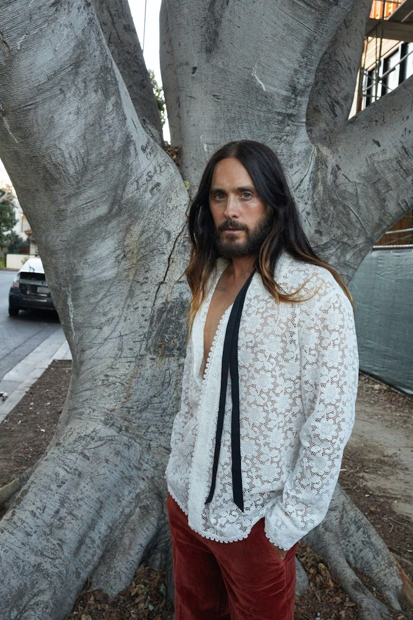 Jared Leto wears a Gucci shirt and pants, standing in front of a tree