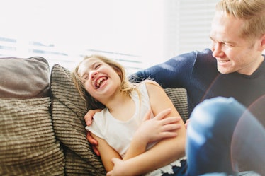 A dad and daughter laughing on a couch.